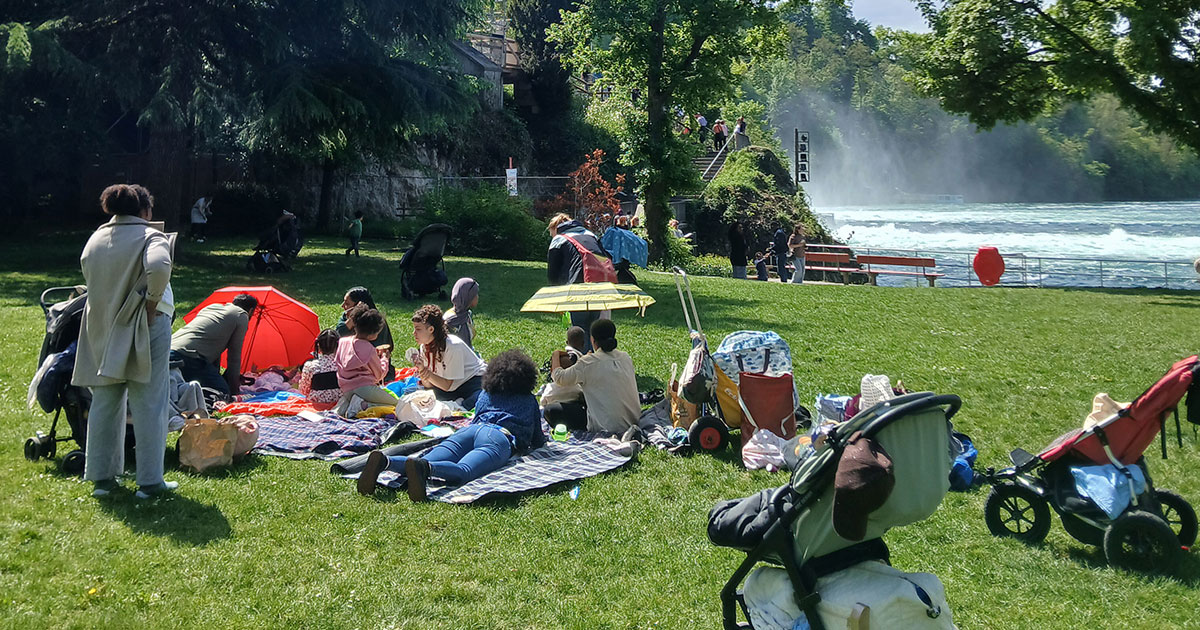Mehrfachbelastete Familien machen mit der Arche Für Familien sitzen beim Picknick am Reihnfall.